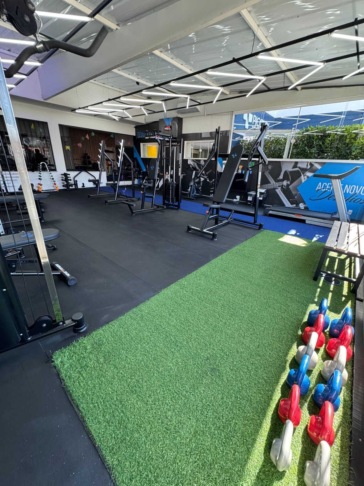 Área externa coberta da academia com grama sintética e kettlebells
